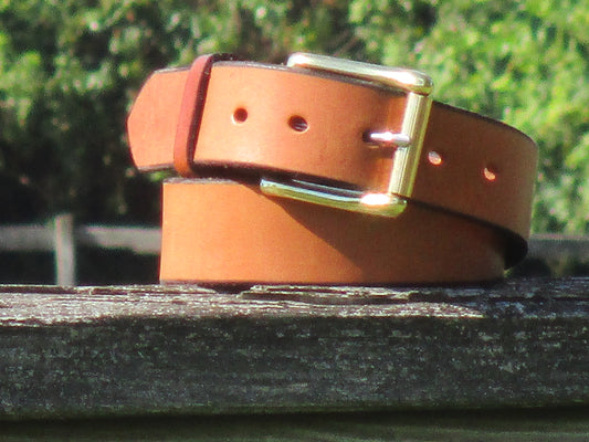 Golden Brown leather belt made from English Bridle Leather, with Solid Brass buckle  on a wooden surface with a blurred green background