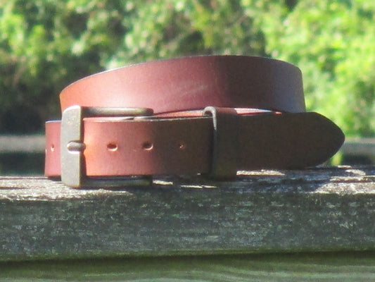 Chocolate Brown leather belt with a Ant Brass buckle on a wooden surface with a blurred green background